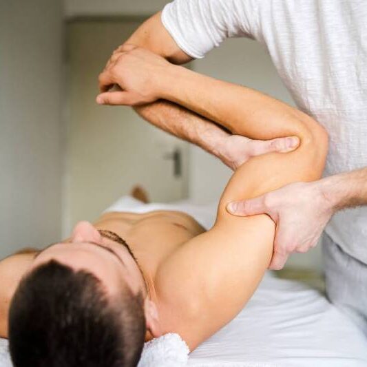 Remedial Massage Therapist conducting a stretching technique on a male client's arm to enhance flexibility and reduce muscle tension during a professional massage session.