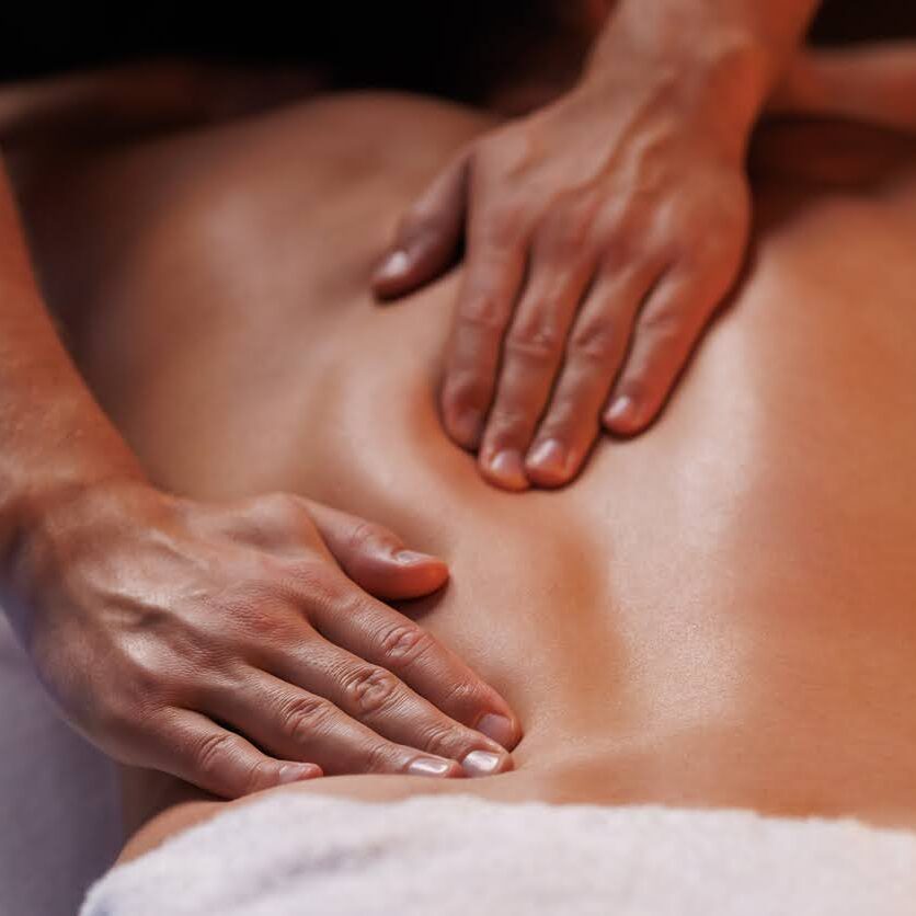 Remedial massage therapist's hands applying a healing touch to the middle and lower back of a client, emphasising gentle pressure to soothe lumbar tension and support spinal health.