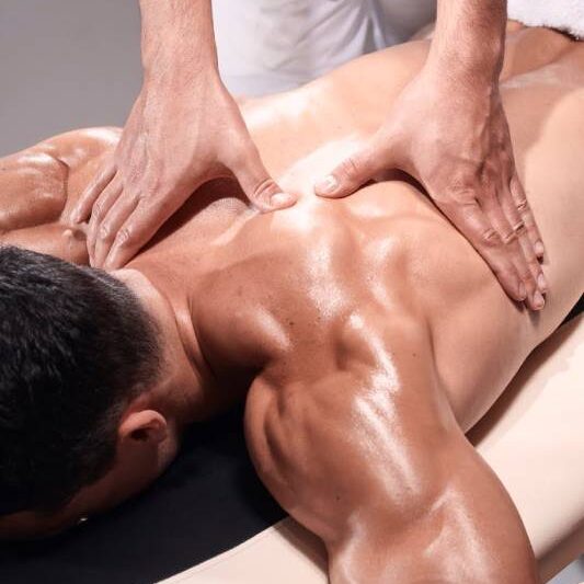 Detail of a remedial massage therapist's hands using precise pressure techniques on the shoulder blades of a male client.